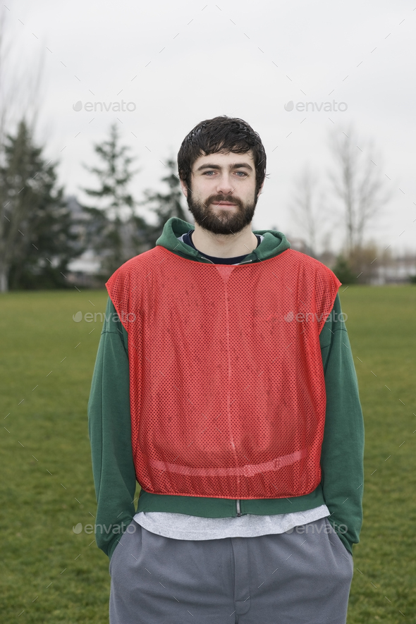 Portrait of a caucasian man playing outdoor sports, wearing a red team vest, hands in pockets.