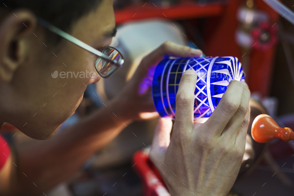A craftsman glass maker holding a vivid blue cut glass cup, inspecting it closely.