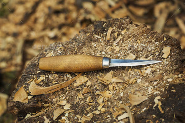 A carving knife with wooden handle lying on splitting block covered in wood shavings.