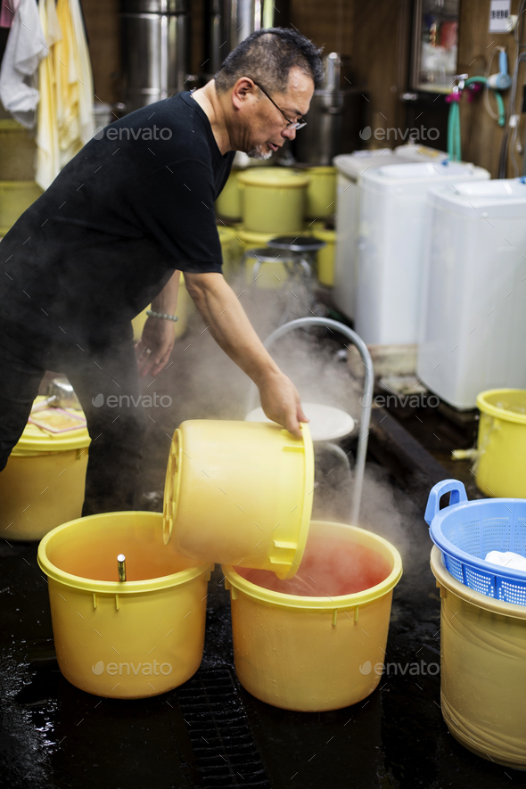Japanese man standing in a textile plant dye workshop, pouring hot water into yellow plastic