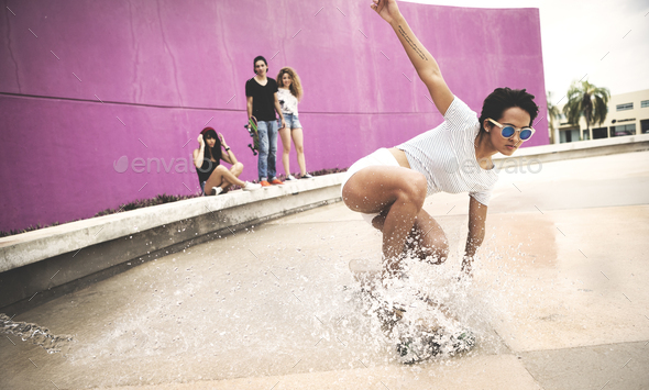 A young woman crouching down on a skateboard to create a water spray.
