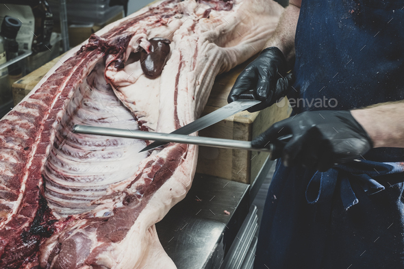 Close up of butcher wearing black rubber gloves working on a pig carcass on butcher\'s block,
