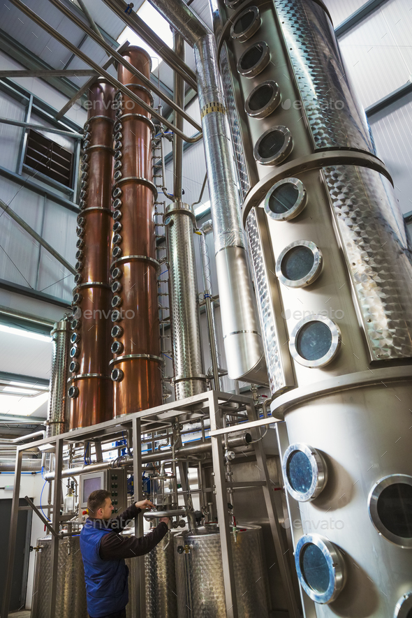 Tall copper distillery chambers in a brewery, brewing storage tanks in copper and steel. A man in - Stock Photo - Images