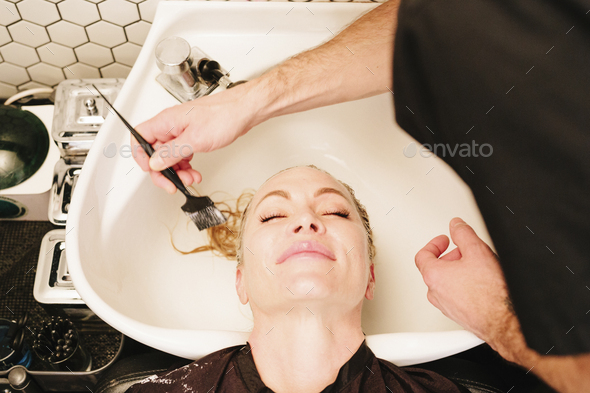 A female client at a hair salon at the basin having a hair treatment applied with a brush. - Stock Photo - Images