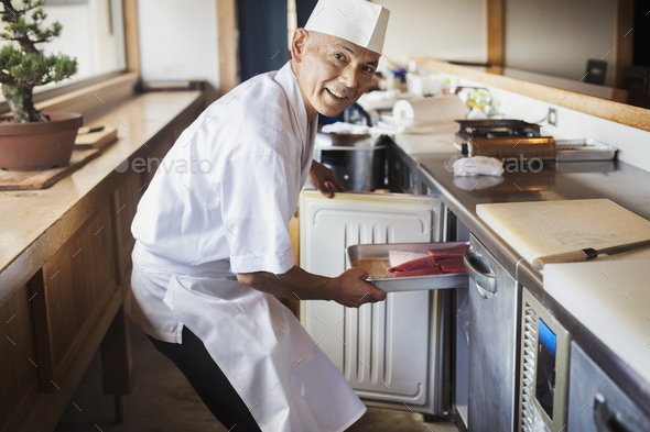 Chef working at a counter at a Japanese sushi restaurant, putting metal tray with fish in