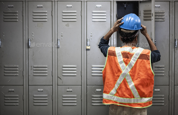 Factory worker wearing a safety vest getting ready for work next to locker in the break room