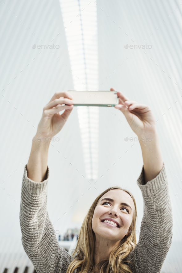 A young woman taking a photograph with her phone, a selfy in the World Trade Centre Oculus building - Stock Photo - Images