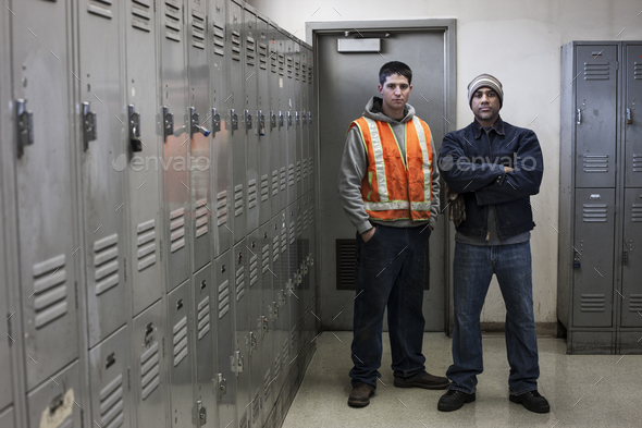 Young caucasian man and a black man factory woker standing next to lockers in a factory break room