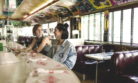 Two young women sitting side by side at a bar counter in a diner.
