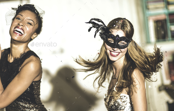 Two young women at a party in sequined dresses drinking and laughing, one wearing a face mask. - Stock Photo - Images