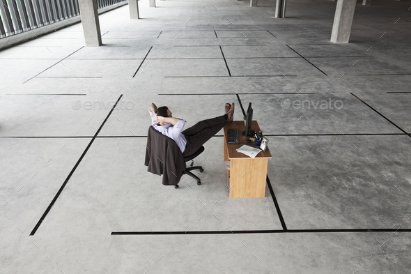 Caucasian businessman at desk looking at a new office layout in a large empty raw business space.