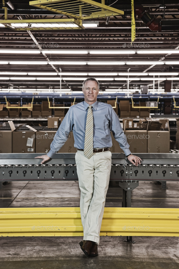 Portrait of a male caucasian executive in a dress shirt and tie next to a motorized converyor - Stock Photo - Images