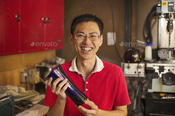 A craftsman in a glass maker\'s workshop holding a shaped glass vase.