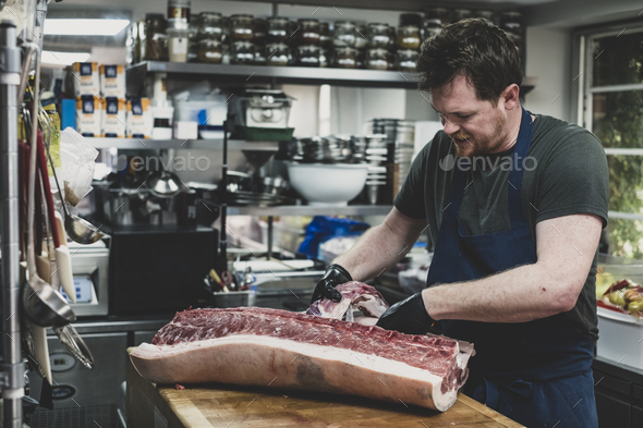 Male butcher wearing apron and black rubber gloves cutting pork ribs on butcher\'s block.