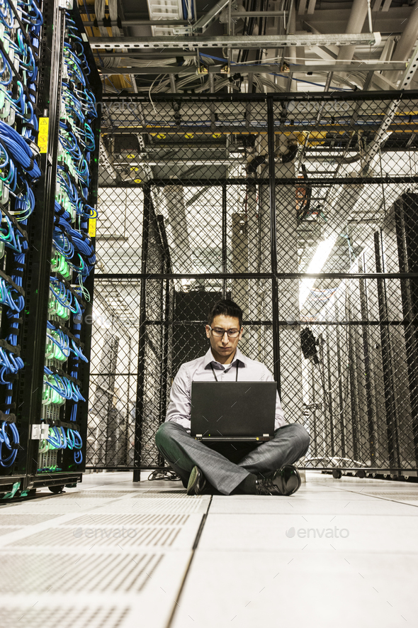 Hispanic man technician doing diagnostic tests on computer servers in a large server farm.