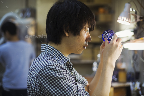 A craftsman at work in a glass maker\'s workshop working on a vivid blue cut glass object.