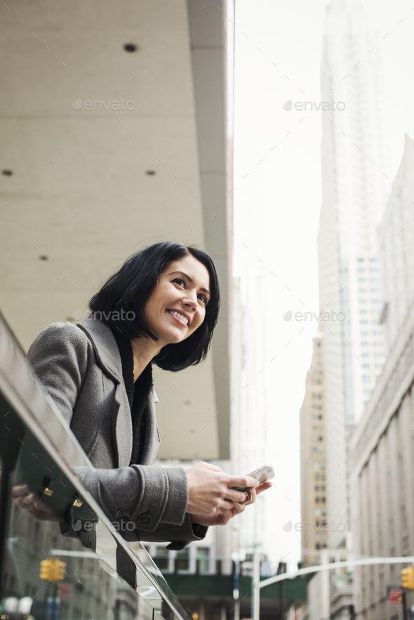 A young woman leaning over a balcony and holding a cellphone, smiling.