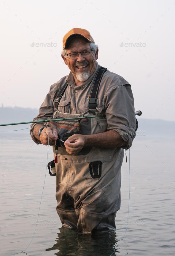 Caucasian senior male tying a fly on his fly fishing line while fishing for salmon and searun - Stock Photo - Images