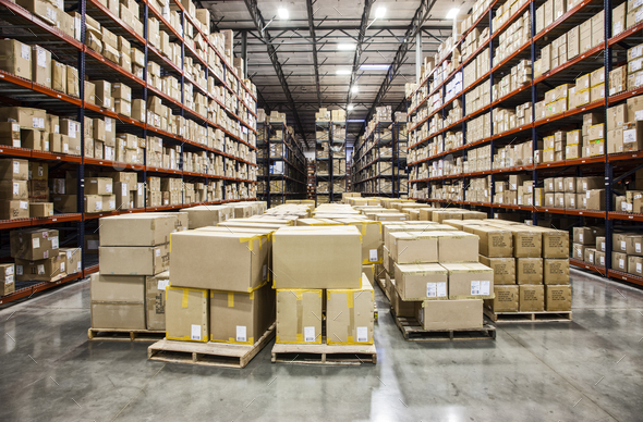 View down aisles of racks holding cardboard boxes of product on pallets  in a large distribution - Stock Photo - Images