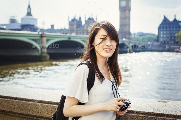 Young Japanese woman enjoying a day out in London, standing on the Queen's Walk by the River Thames.