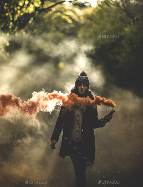 A young woman waving an orange smoke flare in a forest.