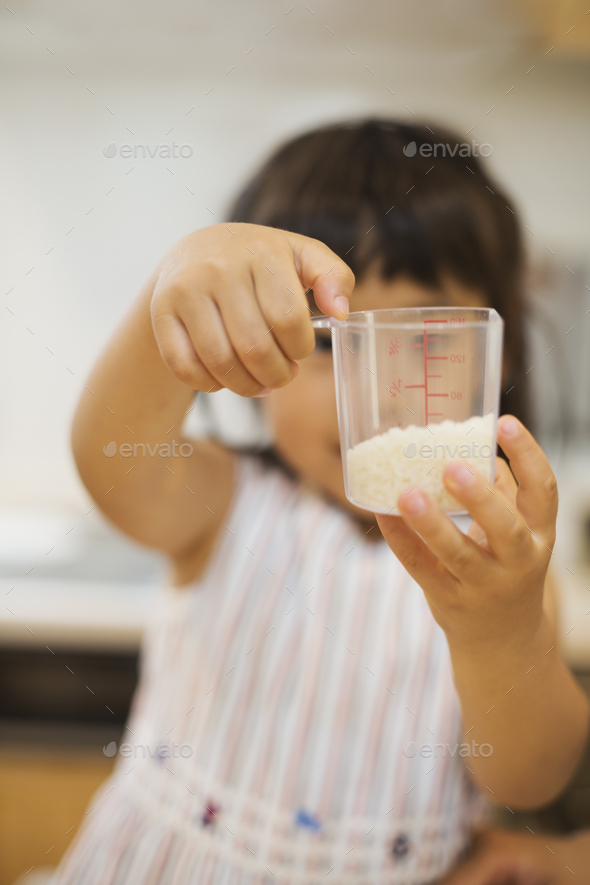 Family home. A child holding a measure of dry rice in a plastic cup.