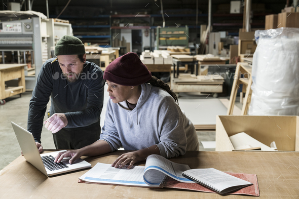 A Caucasian male carpenter and a Black female carpenter working on a laptop computer after work - Stock Photo - Images