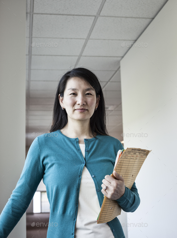 Asian woman holding paperwork in an office hallway.