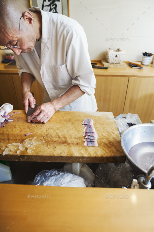 A chef working in a small commercial kitchen, an itamae or master chef slicing fish with a large