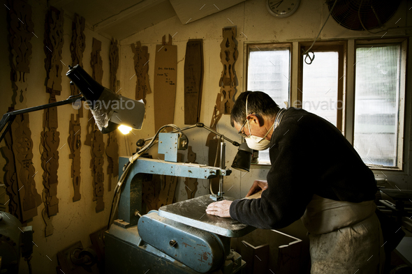 A man working in a furniture maker\'s workshop, using a machine saw.