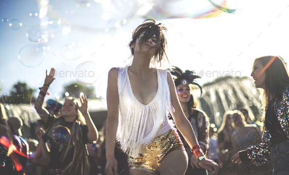 Young woman at a summer music festival wearing golden sequinned hot pants, dancing among the crowd.