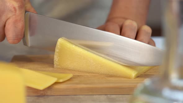 Male Hands Cut with Knife Yellow Parmesan Cheese on Wooden Cutting Board