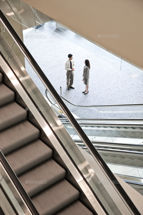 Mixed race pair of business people on the way to a meeting near a set of escalators.