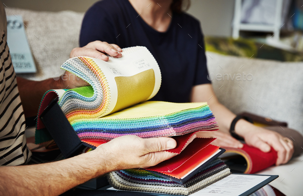 Two people sitting on a sofa, looking at a selection of fabric samples.
