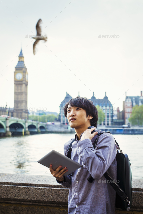 Young Japanese man enjoying a day out in London, standing on the Queen\'s Walk by the River Thames.