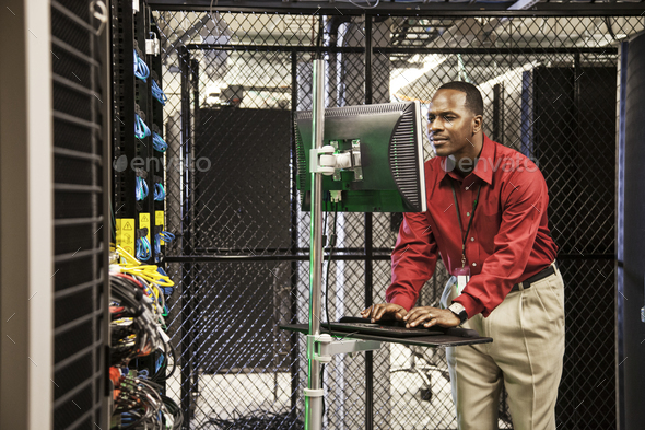 Black man technician doing diagnostic tests on computer servers in server farm.