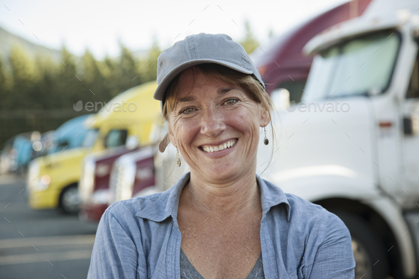 A caucasian woman truck driver near her truck parked in a parking lot of a truck stop.
