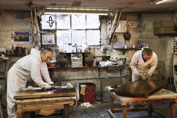 Man standing in a carpentry workshop, wearing protective suit and gloves, applying varnish onto a - Stock Photo - Images