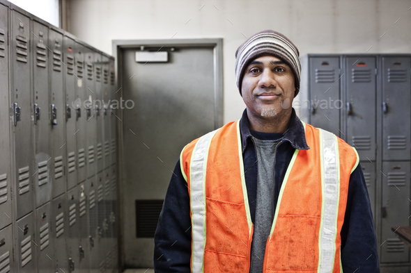 Black man factory worker standing next to lockers in a factory break room.