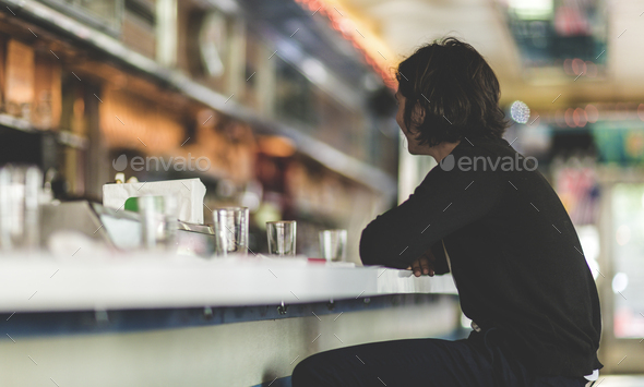Young man sitting on a stool at a bar counter in a diner, back view.