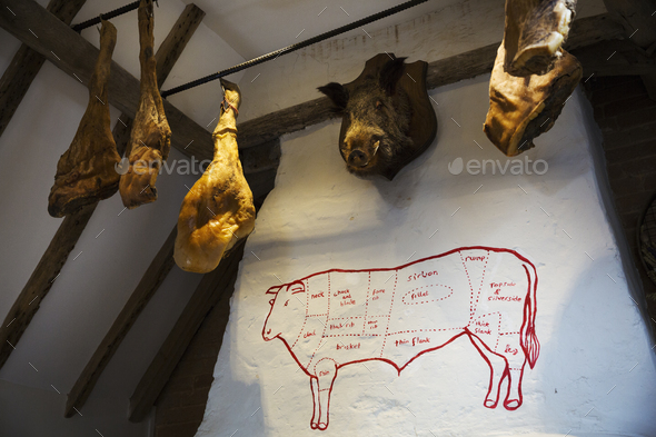 Hams hanging from the ceiling in a butcher's shop, a stuffed boar's head on the wall.