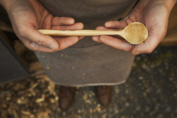 A man\'s hands holding a hand carved wooden spoon with a long tapering handle and smooth round bowl
