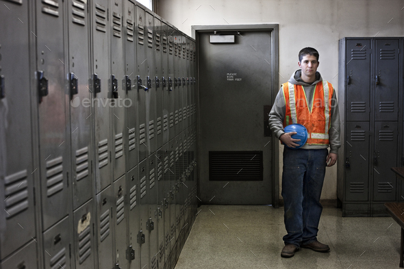 View of a young caucasian factory worker wearing a safety vest and standing next to lockers in a