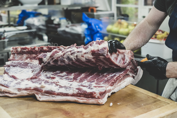 Close up of butcher wearing black rubber gloves cutting pork ribs on butcher\'s block.