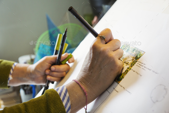 Close up of woman sitting at a drawing board, drawing with a fineliner, using a design template.