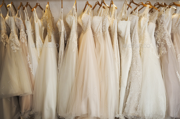 Rows of wedding dresses on display in a specialist wedding dress shop. A variety of colour tones and - Stock Photo - Images
