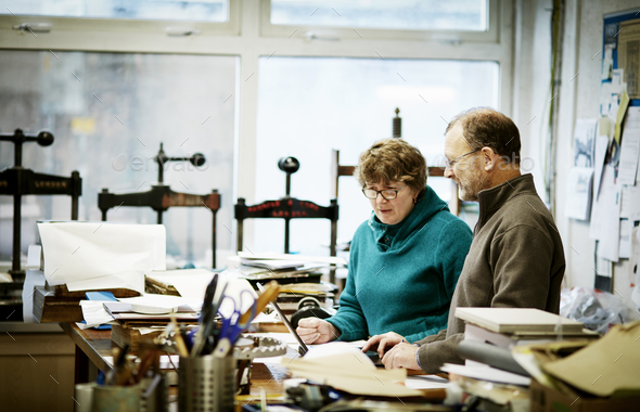 Two people working in a book binding business. Surrounded by tools and book presses.