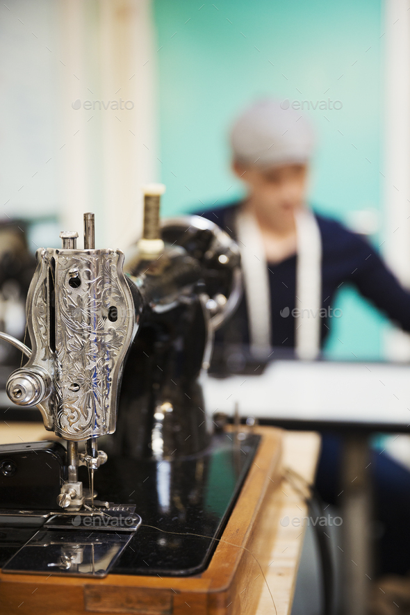 A retro style traditional sewing machine with chased metalwork, and a tailor working in the