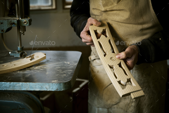 A man working in a furniture maker\'s workshop holding shaped carved chair back struts.