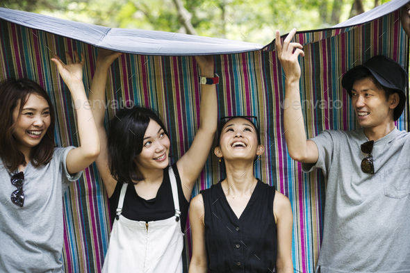 Three young women and man standing in a forest, holding a picnic rug over their heads.
